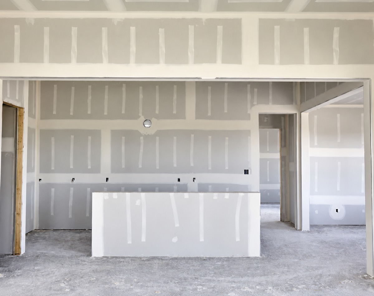 A kitchen under construction with freshly taped drywall seams and joint compound drying over every fastener.